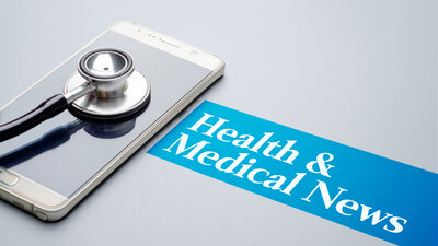 Cell phone laying on a table with a stethoscope on top of it. Sign saying Health & Medical News.