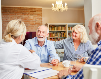 Two older men sitting at a table with an older woman and a woman Physician.