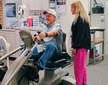 Cardiopulmonary patient riding exercise bike with therapist assisting.